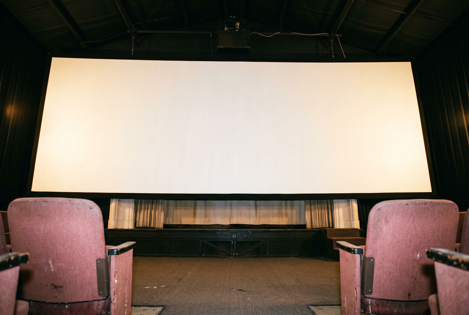 The screen seen from a front-row seat, filling almost the whole view, with the tops of two rose seat backs in the corners of the frame.